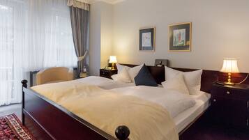 A hotel room with a large bed, two bedside tables, a nightstand, a window with curtains, and two framed pictures on the wall.