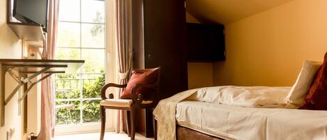 A bedroom with a bed, a chair, a TV, and a window with curtains.