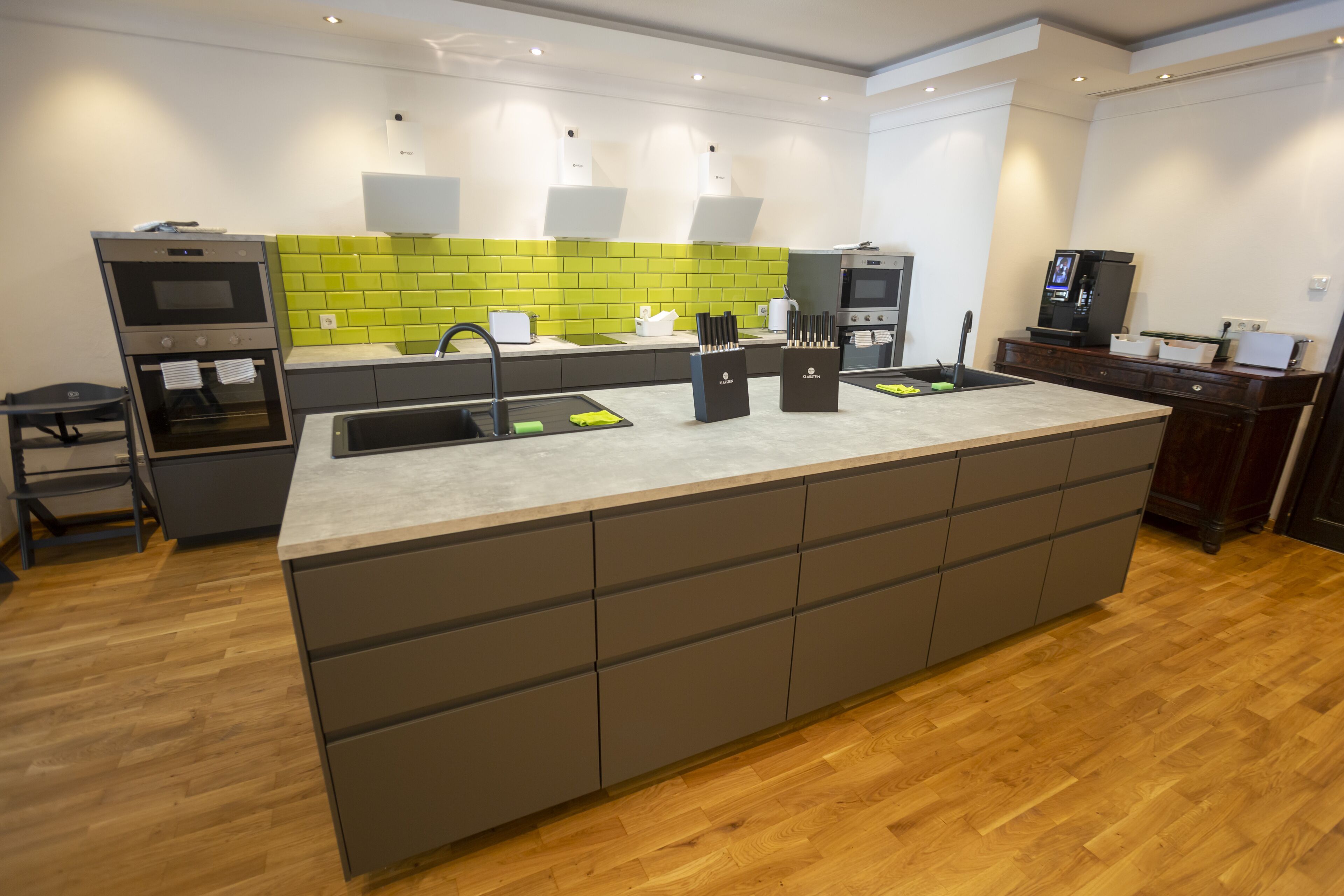 A modern kitchen with a central island, built-in oven, and a green backsplash.