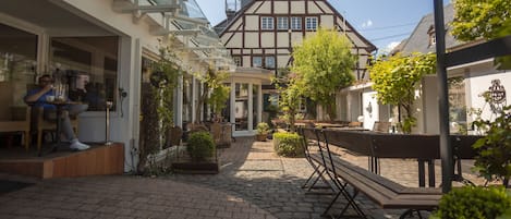 Un patio con un edificio tradicional de entramado de madera, un invernadero de vidrio y zonas de estar al aire libre.