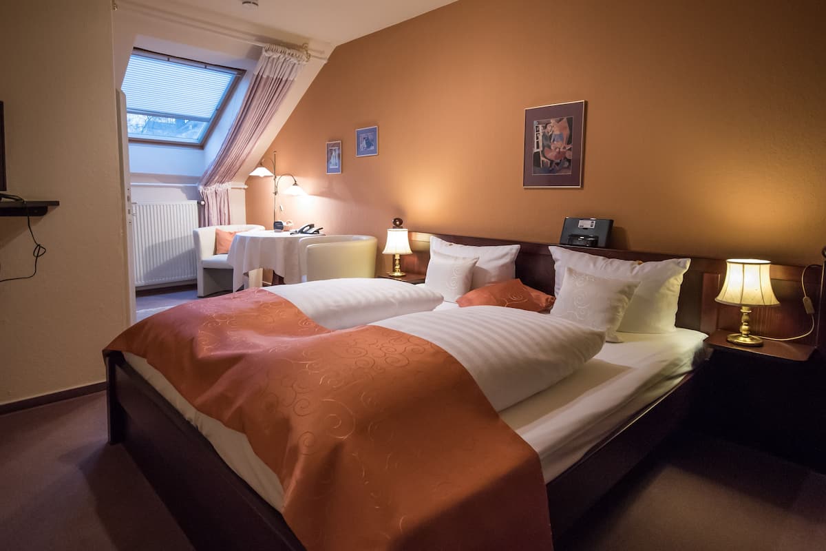 Hotellihuone, jossa on suuri sänky, kaksi yöpöytää, työpöytä ja ikkuna, jossa on verhot.