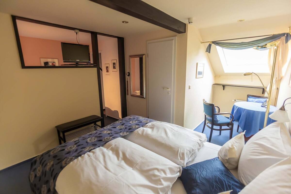 Hotellihuone, jossa on sänky, työpöytä tuolilla, seinälle asennettu televisio ja ikkuna, jossa on verhot.