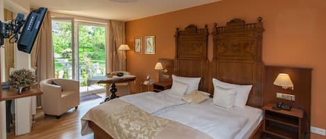 Quarto de hotel com uma cama grande, uma escrivaninha com cadeira, uma mesinha e uma televisão na parede.