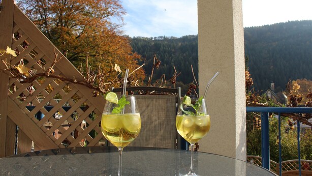 Two glasses of a yellow beverage with mint leaves on a table, set against a backdrop of autumn trees and a mountainous landscape. - The apartment "Loretta" is a modern, quiet and centrally located apartment. (Traben-Trarbach)