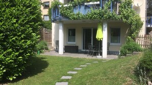 A two-story building with a balcony covered in greenery, a paved patio area with outdoor furniture, and a well-maintained lawn. - The apartment "Loretta" is a modern, quiet and centrally located apartment. (Traben-Trarbach)
