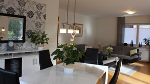 A modern living room with a dining table, chairs, a sofa, and a large window. - The apartment "Loretta" is a modern, quiet and centrally located apartment. (Traben-Trarbach)