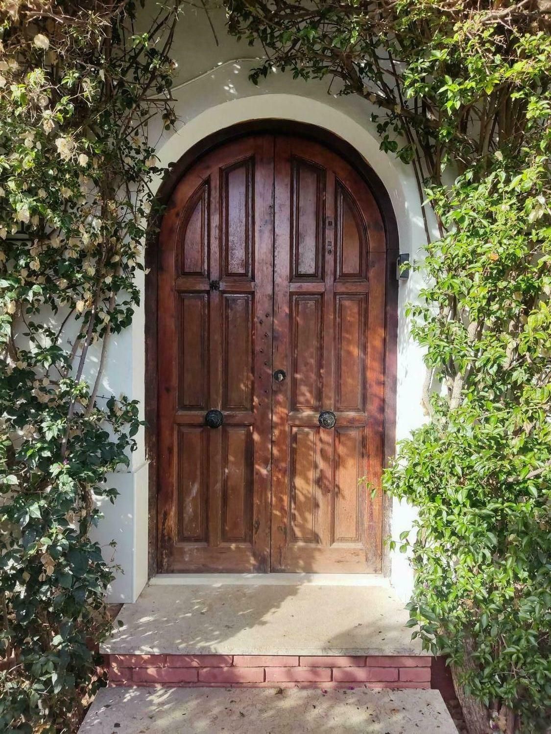 A wooden double door with a white archway, surrounded by greenery.