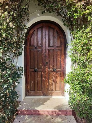 A wooden double door with a white archway, surrounded by greenery.