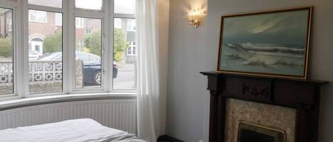 A hotel room with a large window, a fireplace, and a painting on the wall.