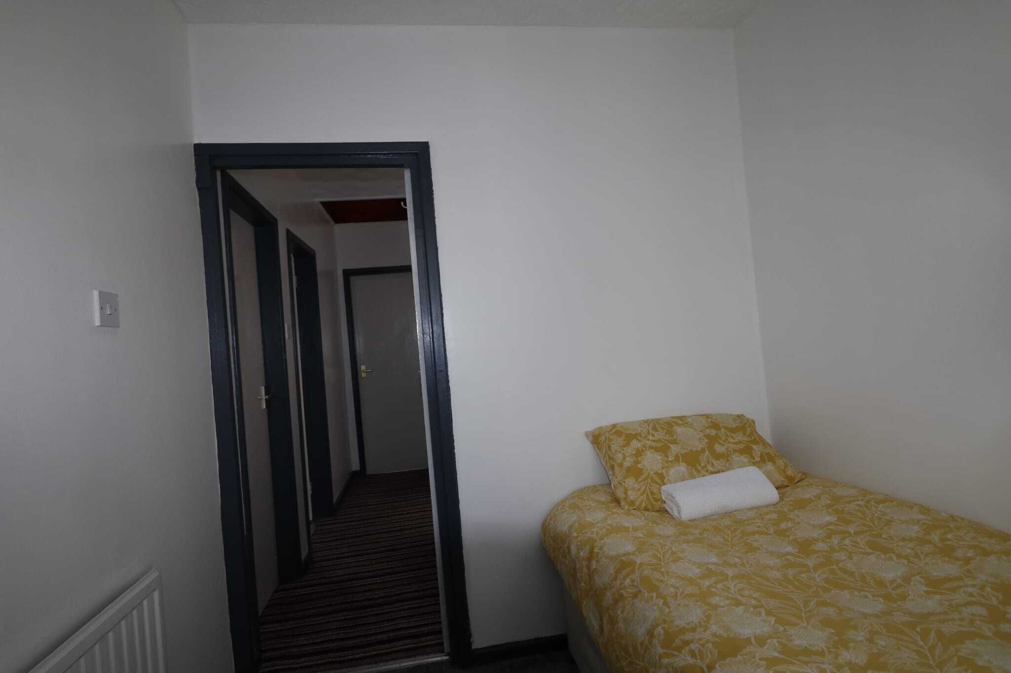 Une petite chambre avec un lit simple, une couvre-lit à motifs, un oreiller blanc et un miroir au mur.