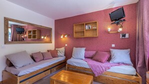 Une pièce confortable avec deux lits en bois, une table en bois, un téléviseur fixé au mur et un miroir.