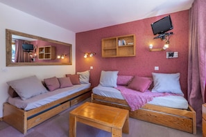 Quarto acolhedor com duas camas de madeira, uma mesa de madeira, TV fixada na parede e um espelho.