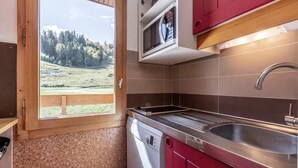 Une cuisine compacte dotée d’un four à micro-ondes encastré, d’un évier en acier inoxydable et offrant une vue sur un paysage boisé grâce à une grande fenêtre.