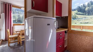 Une cuisine de taille réduite, équipée d’un réfrigérateur, d’une table en bois et de chaises.