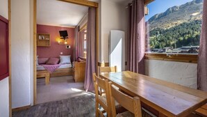 Une chambre de taille modeste, comprenant un lit, une petite table et une fenêtre donnant sur une vue sur les montagnes.