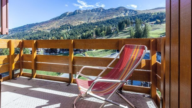Un balcon doté d’une balustrade en bois, d’un fauteuil suspendu à rayures et offrant une vue sur un paysage montagneux.