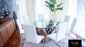 A modern conference room with a glass table surrounded by white chairs, a brown leather couch, and a large plant.
