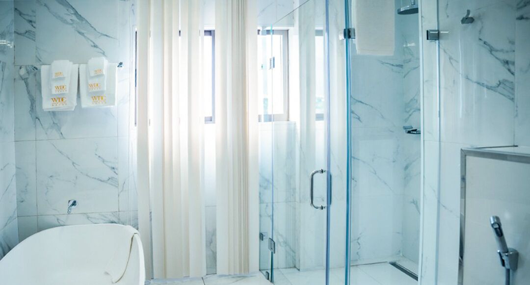 A modern bathroom with a glass shower enclosure, a white bathtub, and marble walls.