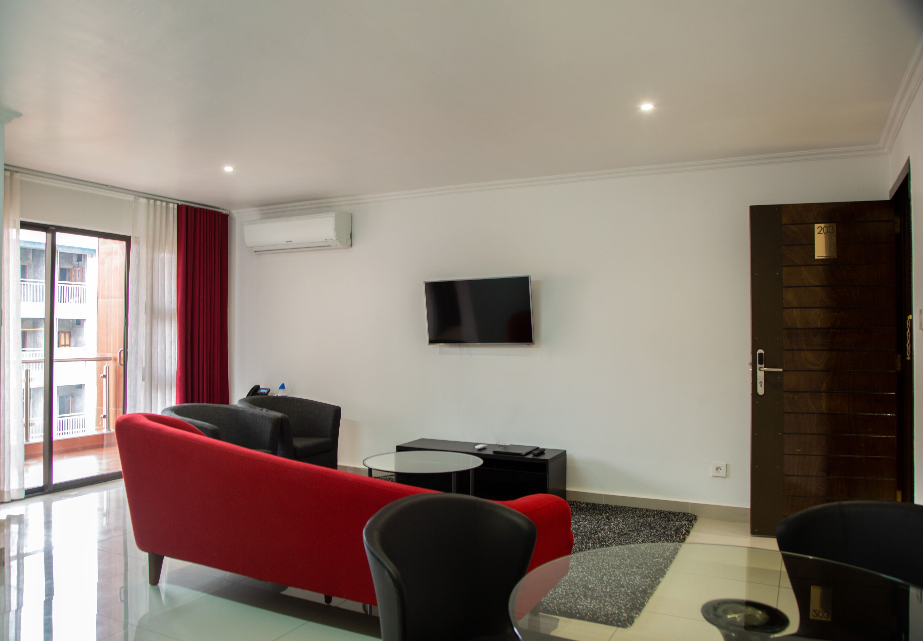 A modern living room with a red sofa, black armchairs, a small round table, and a flat-screen TV mounted on the wall.