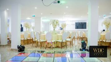 A banquet hall with round tables, white chairs, and floral centerpieces.