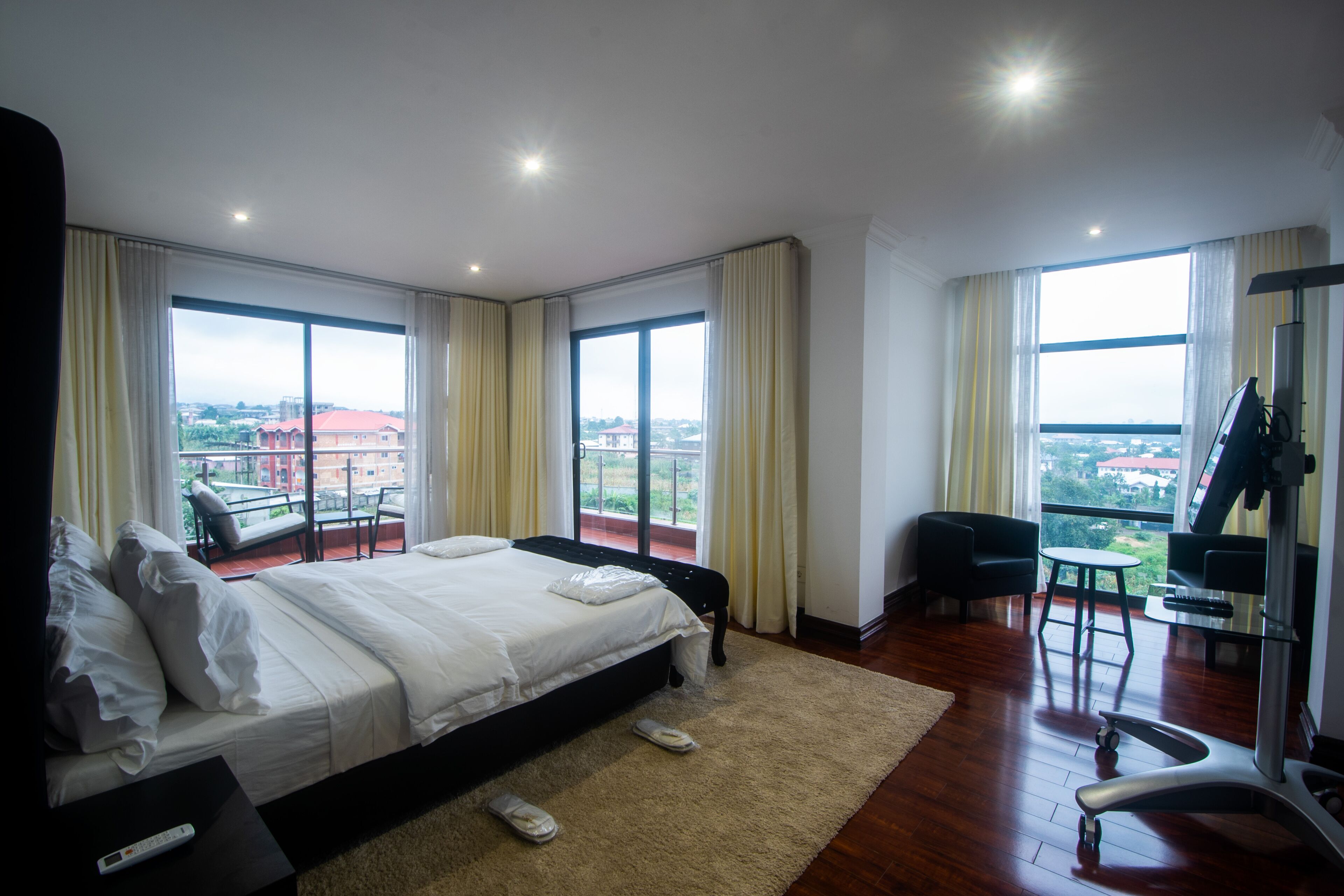A hotel room with a large bed, a TV, a treadmill, and a balcony with a view of the city.