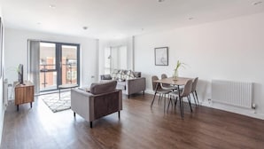 A spacious living area with a sofa, chairs, a dining table, and a large sliding glass door leading to an outdoor balcony. - Stay Zeni, Ouse Court York Contemporary 2 Bed Flat (York)