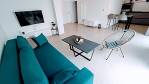 Un salon moderne avec un canapé de couleur turquoise, une table basse, un fauteuil suspendu et un téléviseur à écran plat fixé au mur.