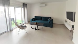Un salon moderne avec un canapé de couleur turquoise, une table basse, un fauteuil en osier et un téléviseur fixé au mur.