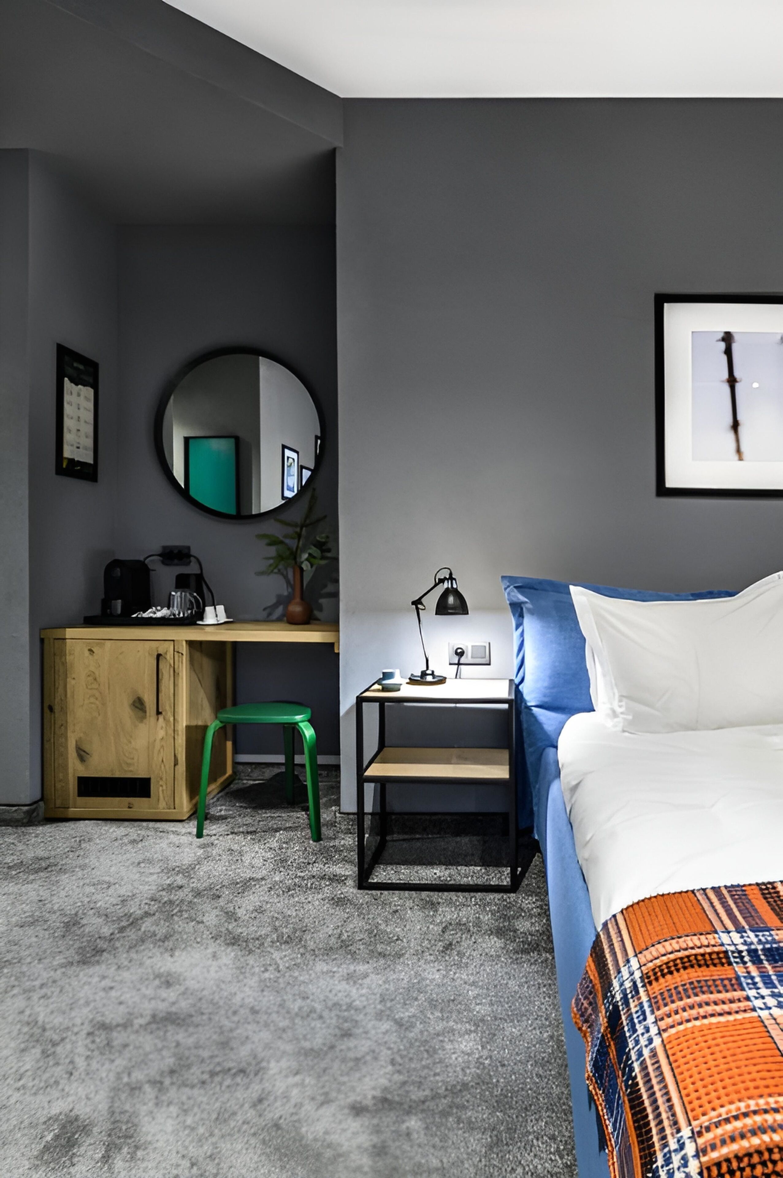 Ein modernes Schlafzimmer mit Bett, Schreibtisch, Stuhl, Nachttisch, Lampe, Spiegel und einem gerahmten Bild an der Wand.