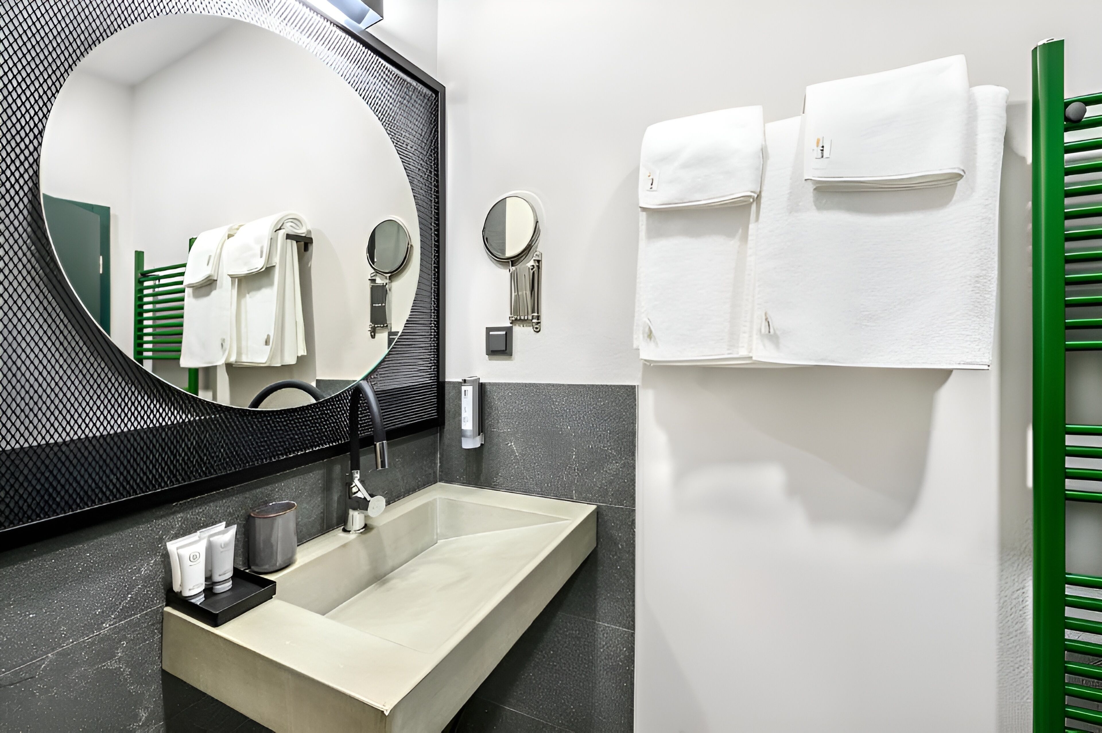 Un baño moderno con un espejo grande, un lavamanos y varios toallas en un perchero.