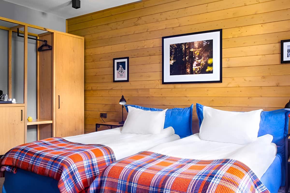 A bedroom with a wooden wall, a bed with white and blue pillows, and a plaid blanket.