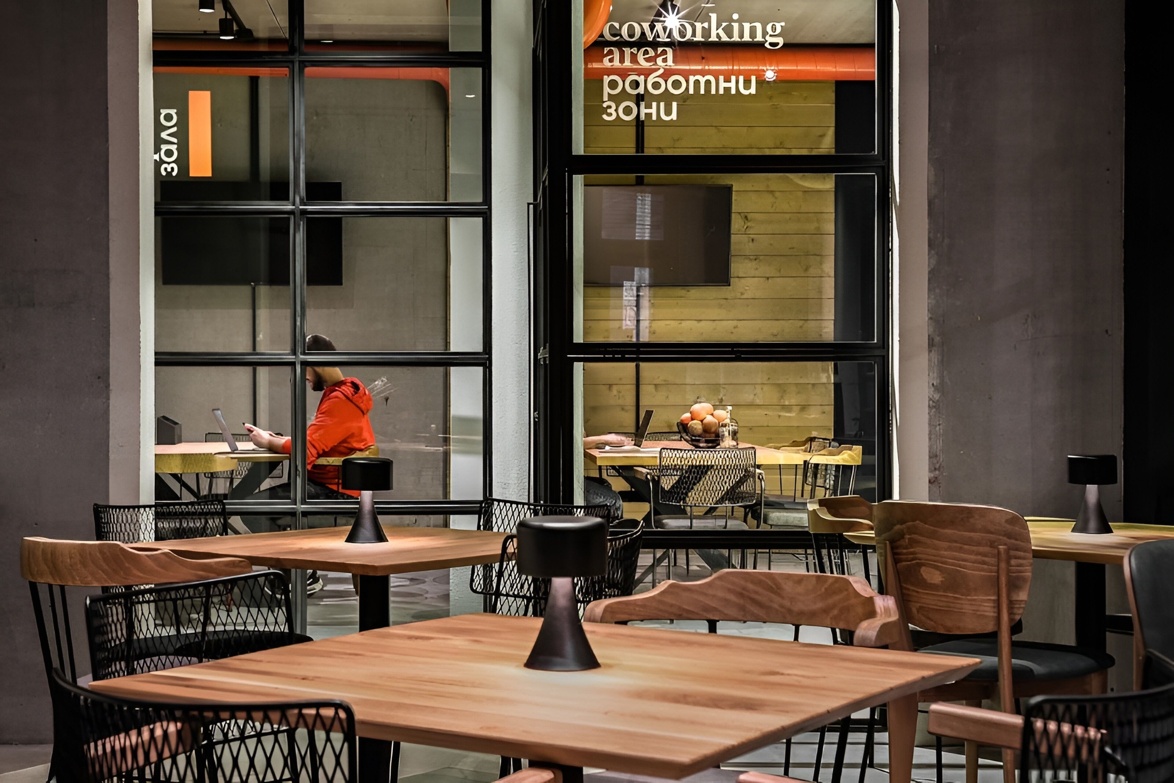 Un espacio de coworking con mesas y sillas, una persona trabajando en una mesa, y un cartel que indica la zona de coworking.