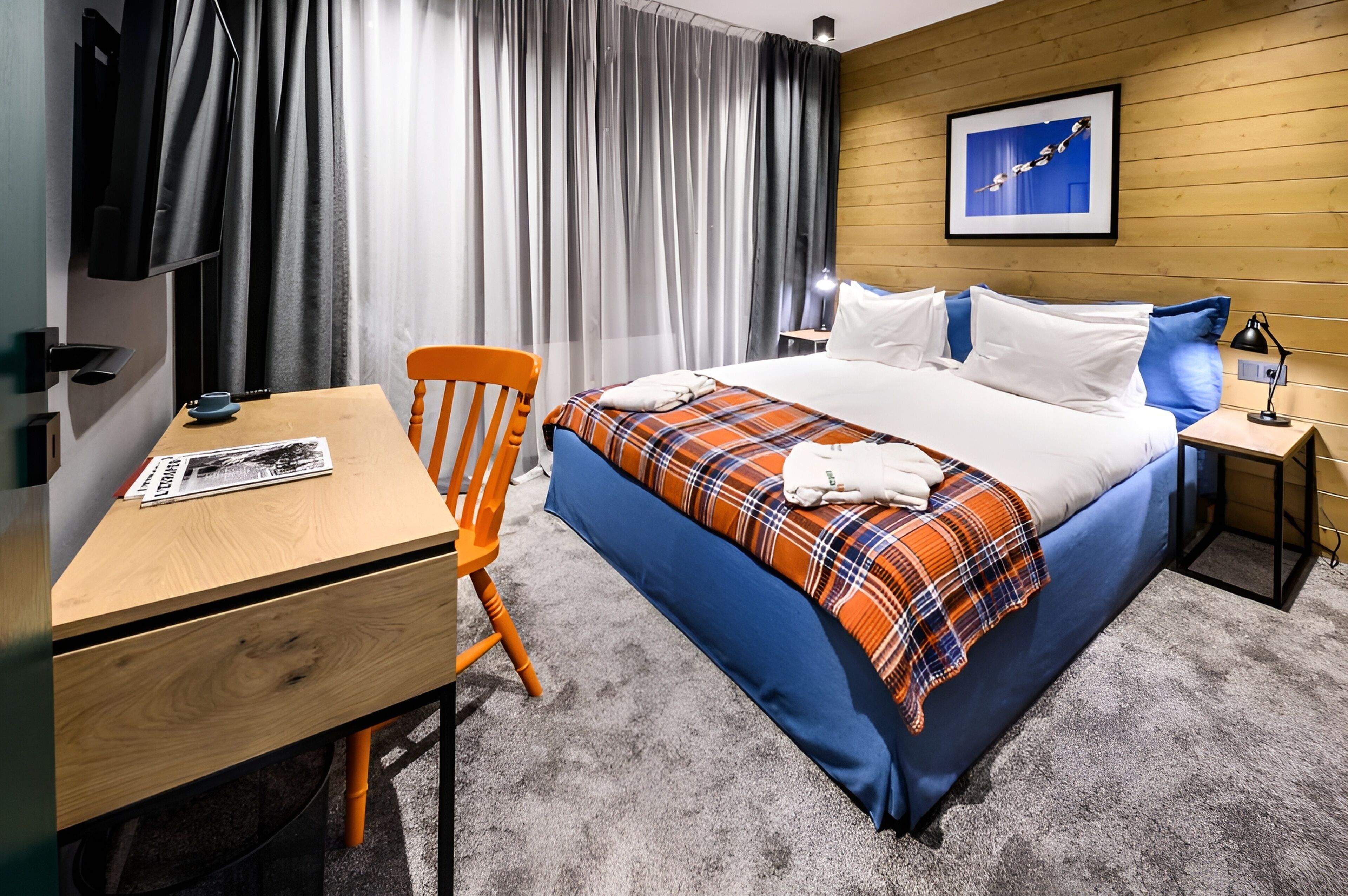 A hotel room with a bed, a desk, a chair, a TV, and a picture on the wall.