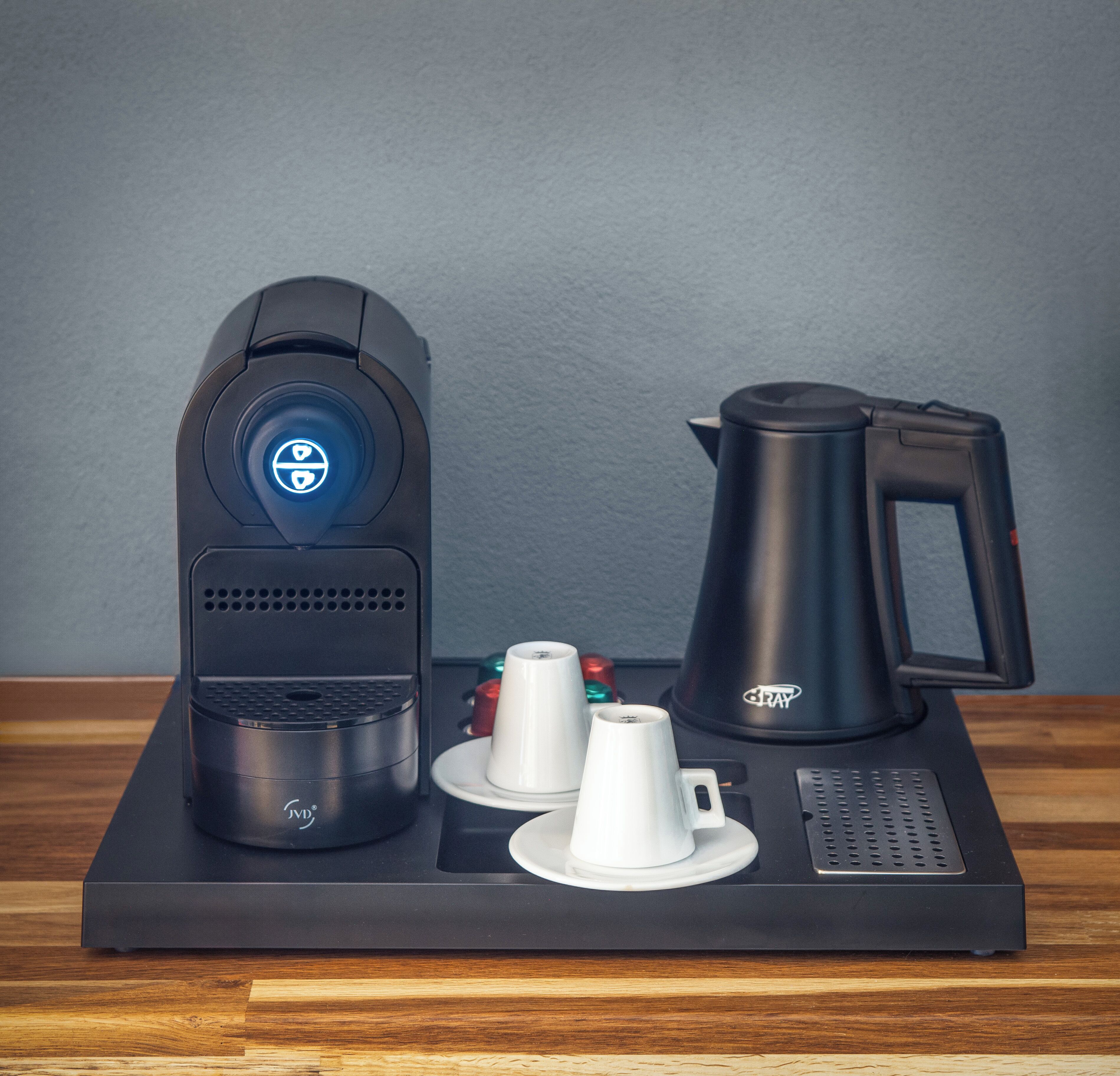 Una máquina de café con pantalla digital, un hervidor y dos tazas blancas sobre una bandeja negra.