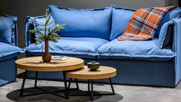 A blue sofa with a plaid throw pillow, two round wooden tables, and a small potted plant.
