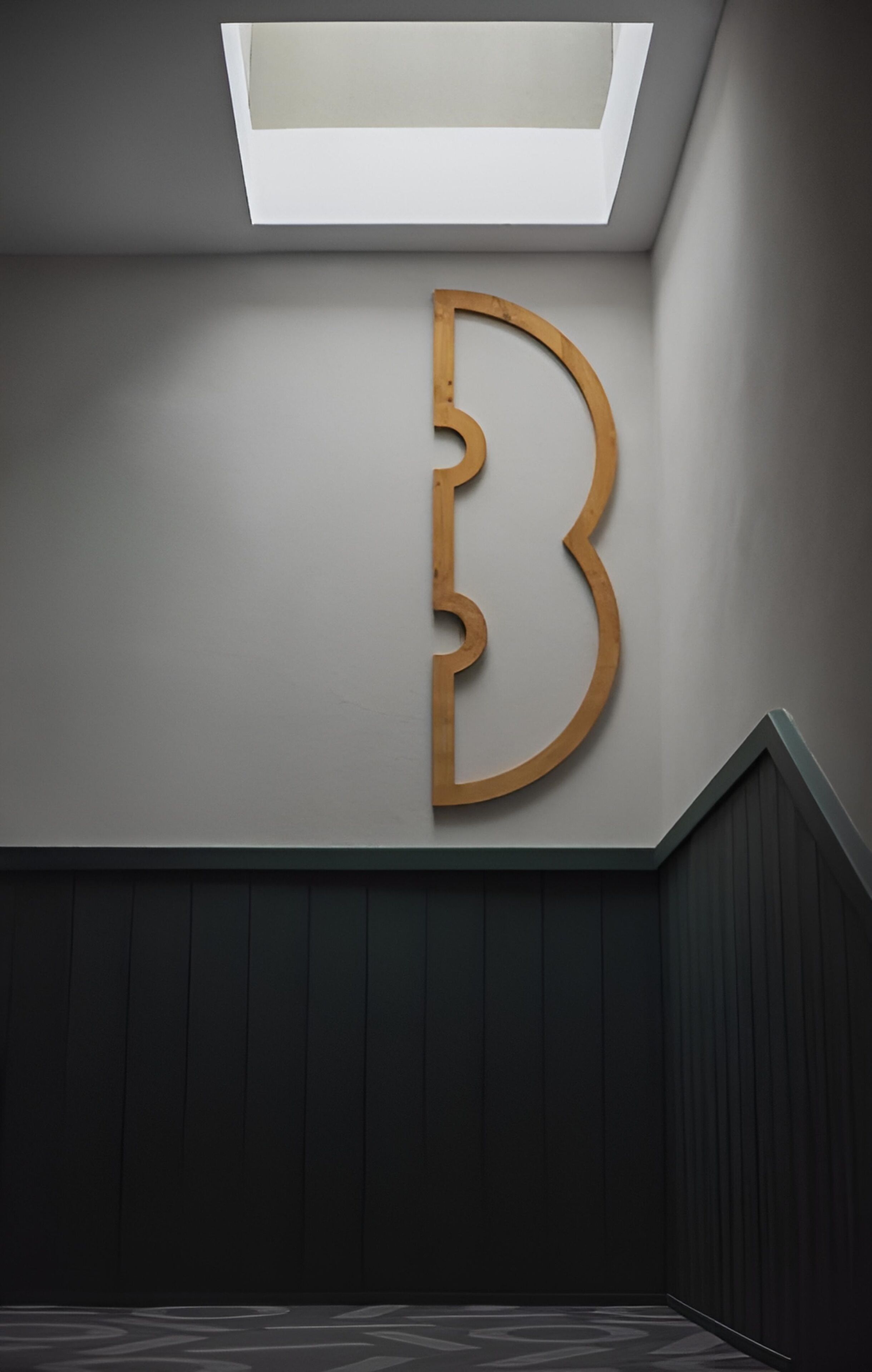 Un intérieur moderne, avec un grand panneau en bois en forme de « B » sur le mur, un plafond en pente et un lambris en bois foncé.