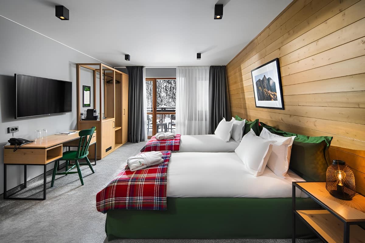 A hotel room with a bed, a desk, a chair, a TV, and a window with curtains.