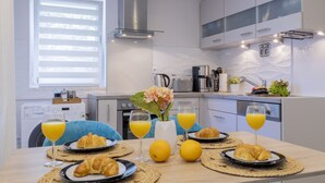 A modern kitchen with white cabinets, a stainless steel range hood, and a window with blinds.
