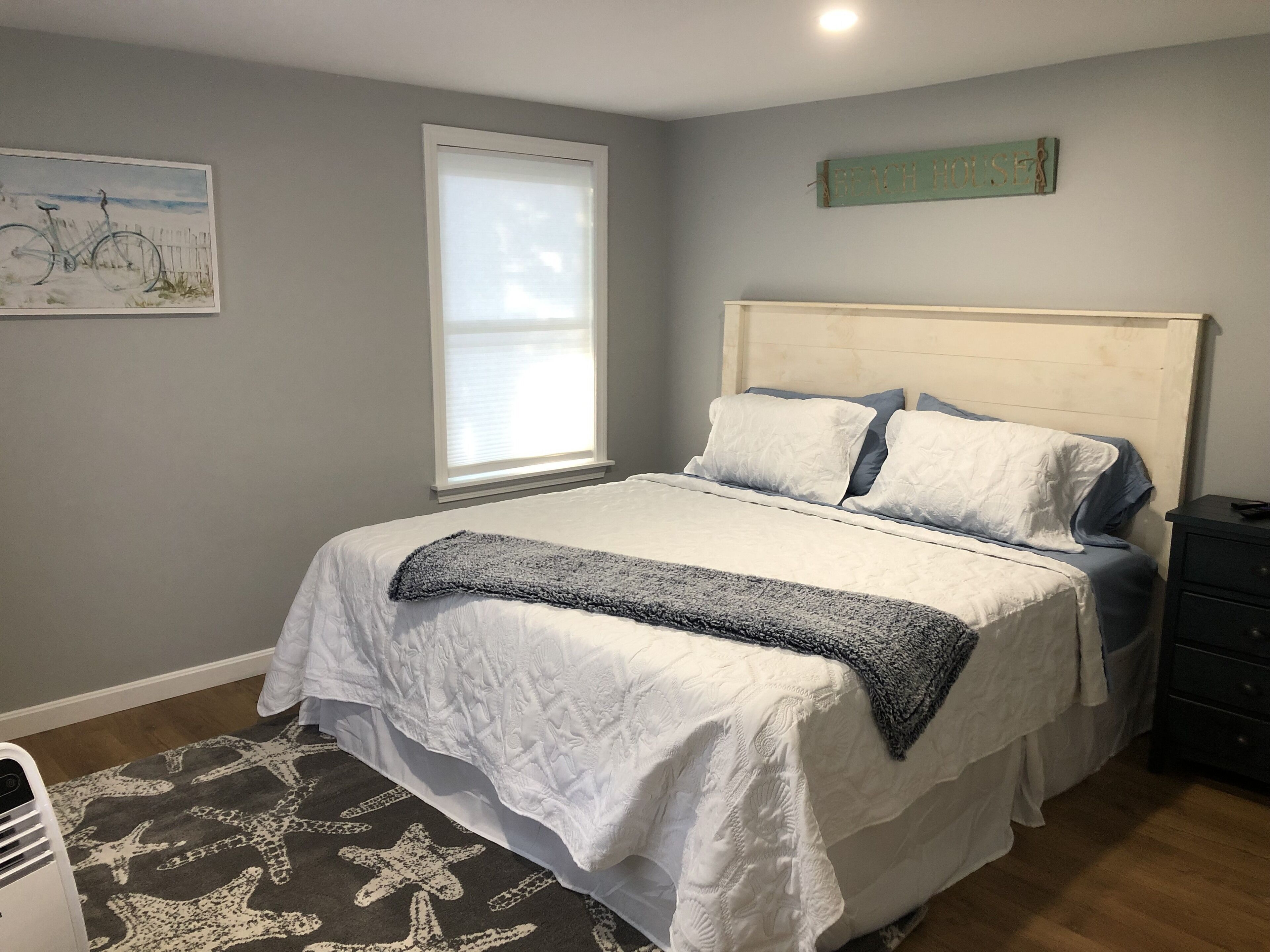 Ein Schlafzimmer mit Bett, Fenster, einem an der Wand befestigten Schild und einer Stehlampe.