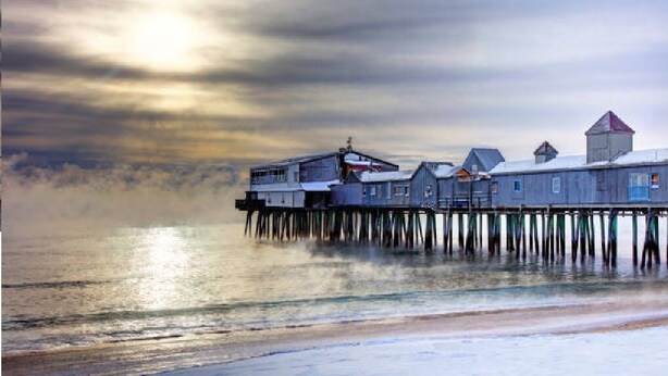 A pier with buildings extending over the water, featuring a prominent structure with a red roof. - Beautiful 4 Bedroom short walk to the Pier, Beach, & Attractions (Old Orchard Beach)