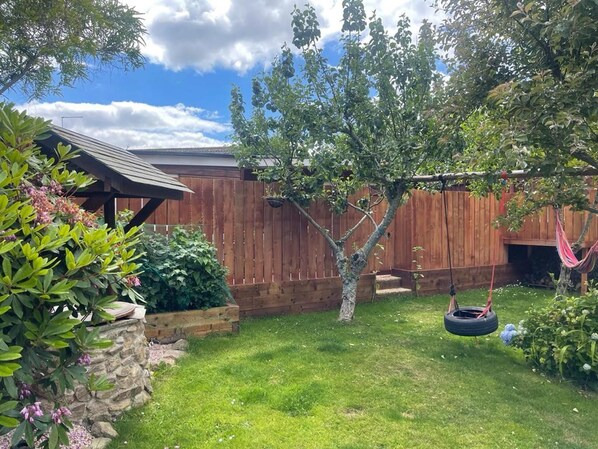 A backyard with a wooden fence, a swing set, and a hanging tire swing.