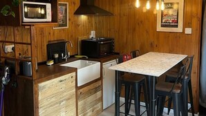 A compact kitchen with wooden walls, a white countertop, a sink, a stove, and a dining table with four chairs. - Charming Chalet - Sleep 3/4 & Free Parking (Dartmouth)
