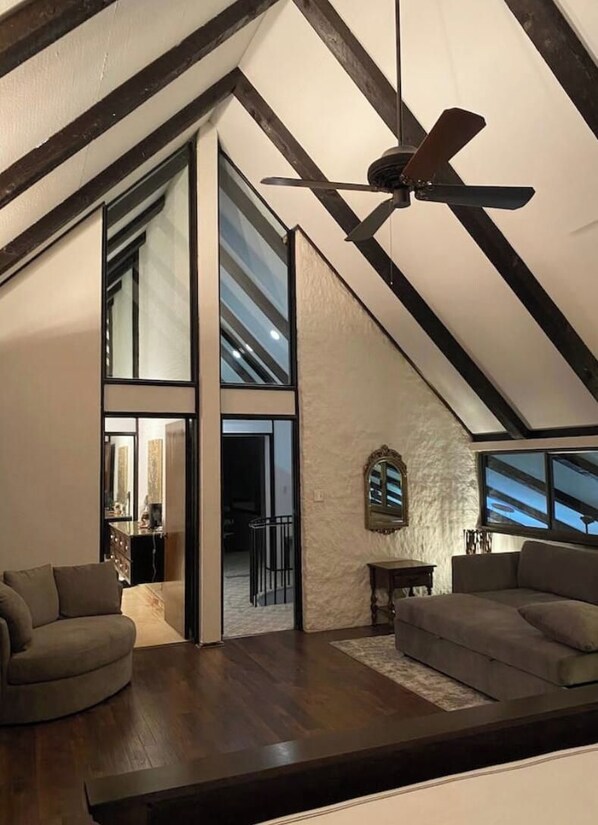 A modern loft-style room with a sloped ceiling, a ceiling fan, and a large window. - Family vacation house (Enid)