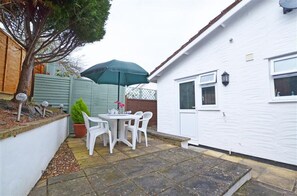 A patio with a table and chairs, a green umbrella, and a white building with a window and door.