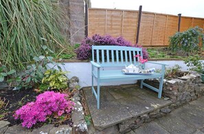 A blue bench with a tray of tea and a teapot, surrounded by flowering plants and a stone wall.
