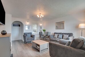 A modern living room with grey sofas, a coffee table, and a dining area with chairs and a table.