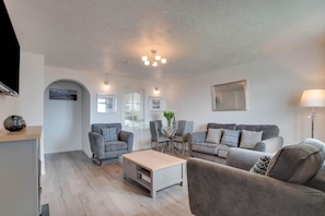 A modern living room with grey sofas, a coffee table, and a dining area with chairs and a table.