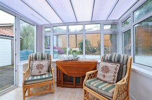 A conservatory with wicker furniture, a wooden table, and large windows.