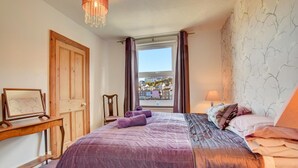 Un dormitorio con cama, una silla, un escritorio, una ventana con cortinas y vistas a edificios.