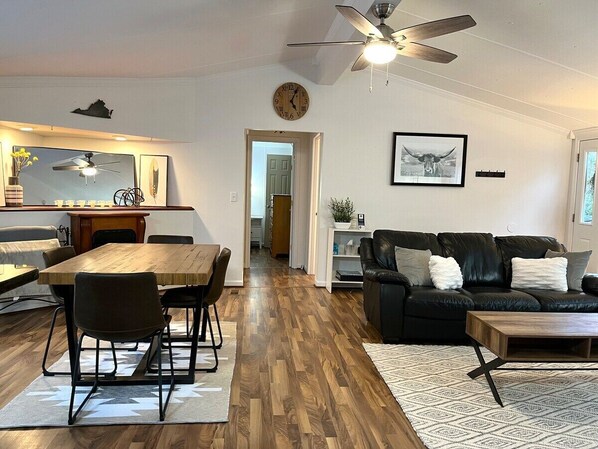 A modern living room with a wooden dining table, black leather sofa, and a ceiling fan. - Everley Whole Property (Afton)